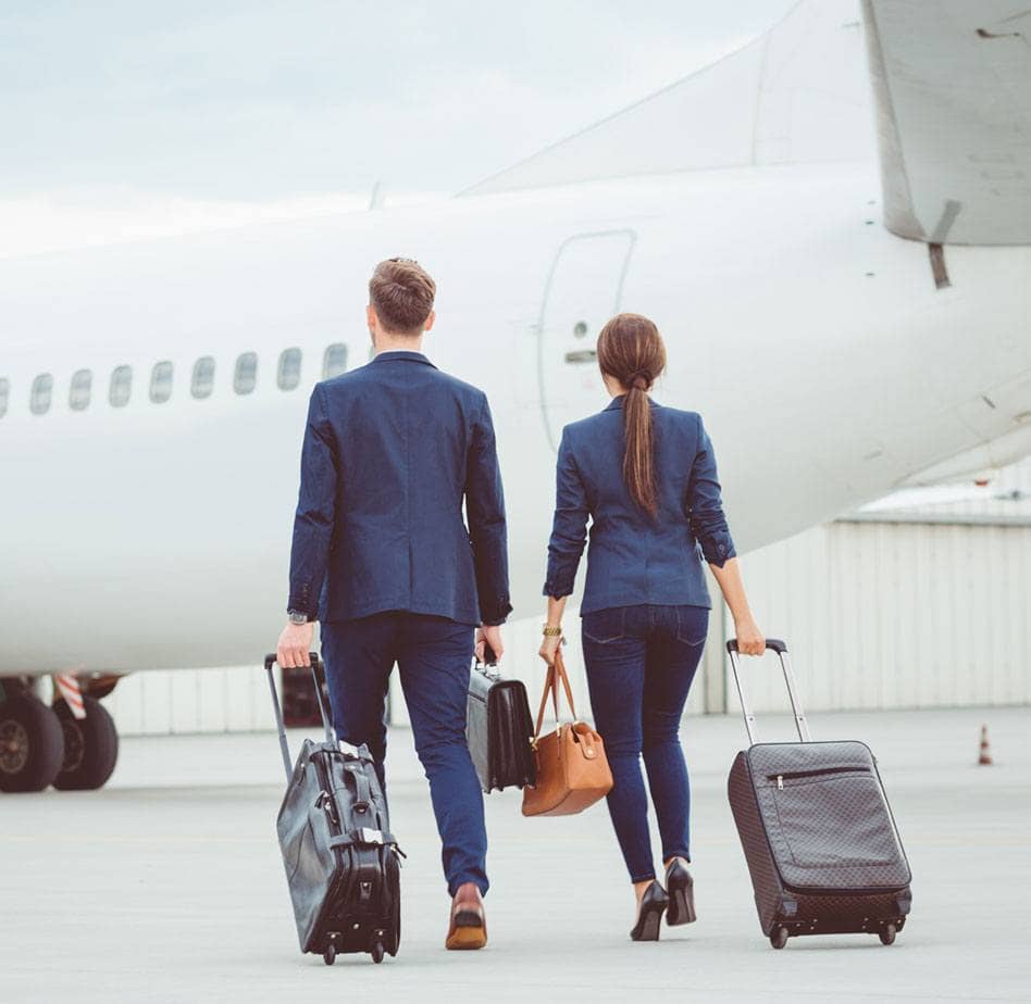 Two business colleagues with luggage walking together on tarmac towards the airplane