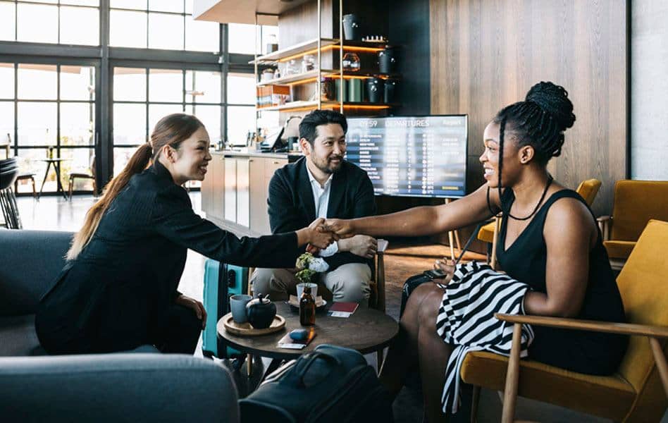 Asian female travel consultant shaking hands with woman of colour entrepreneur and her asian male business partner at the airport lounge