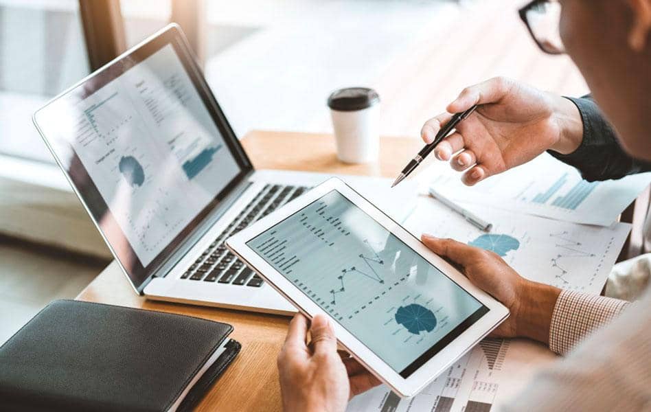 Travel consultant going through travel management reports with businessman using tablet and laptop