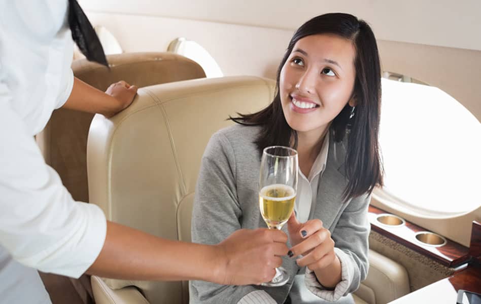 Air stewardess offering a glass of wine to asian businesswoman in airplane
