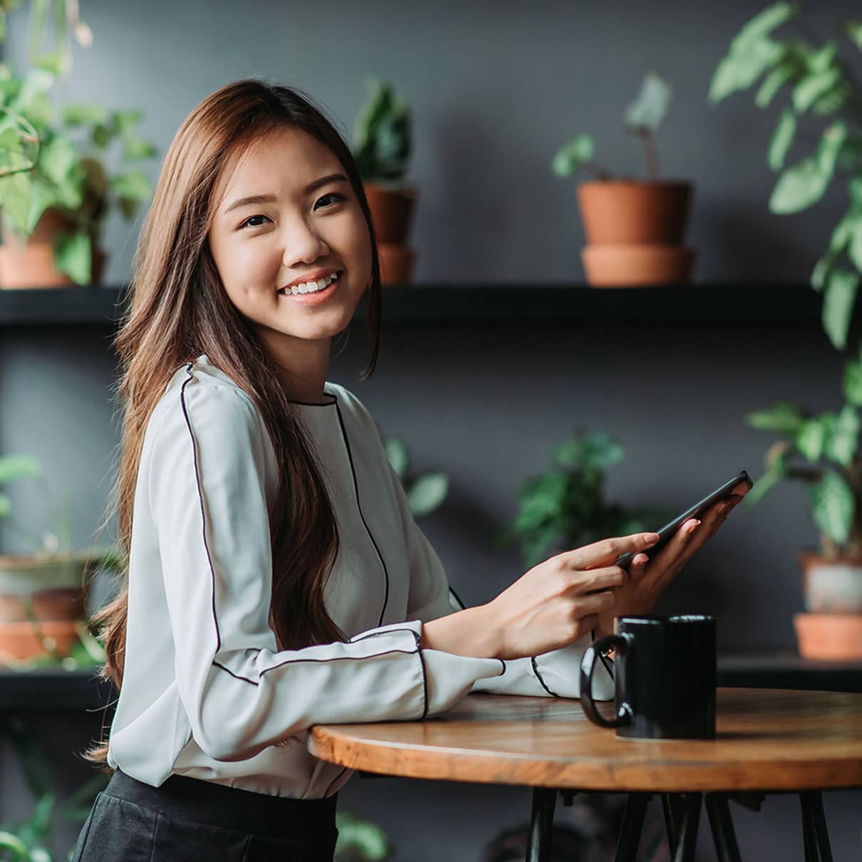 Smiling asian female executive having coffee break and using phone in the office pantry